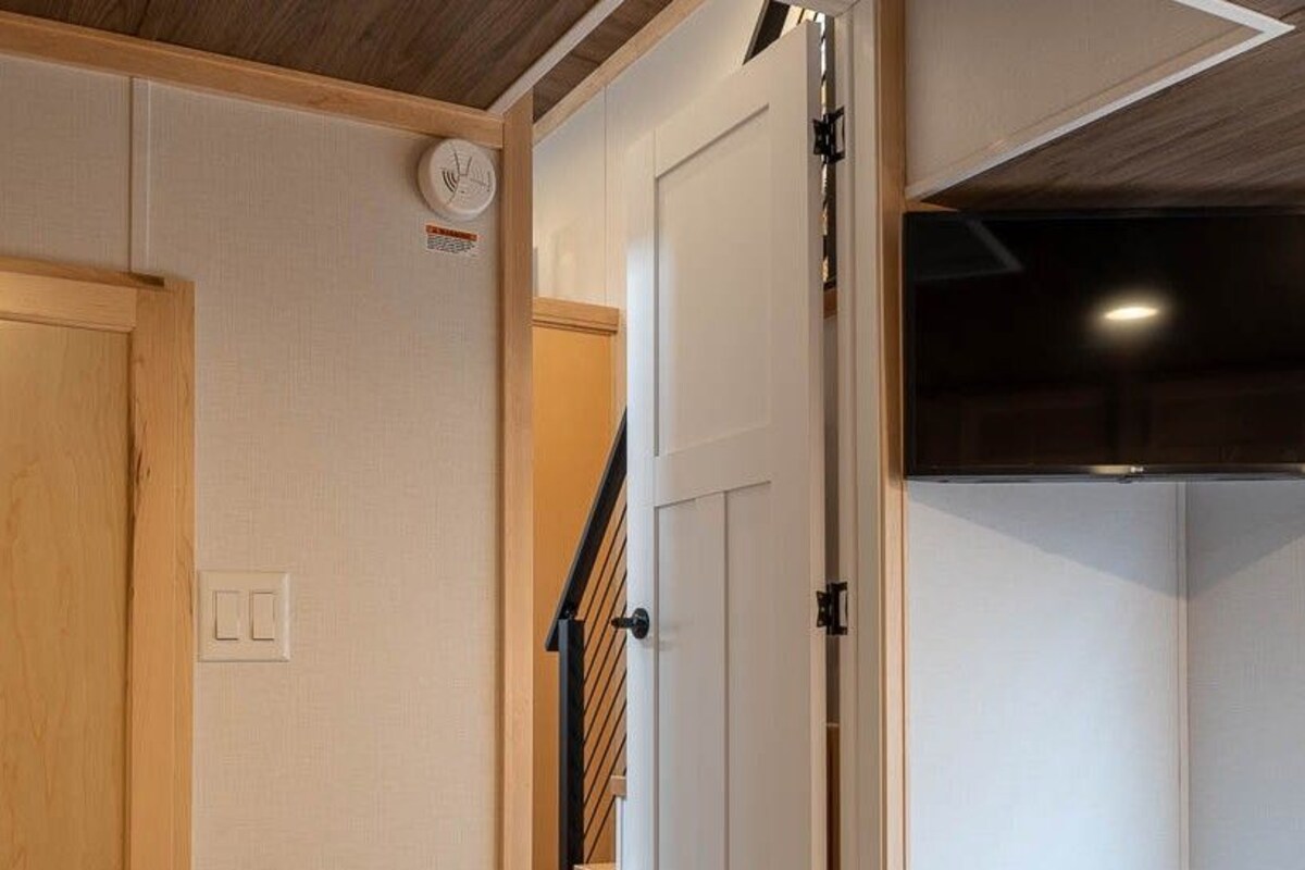 A room with a bed, a door, a light switch, and a wall-mounted clock.