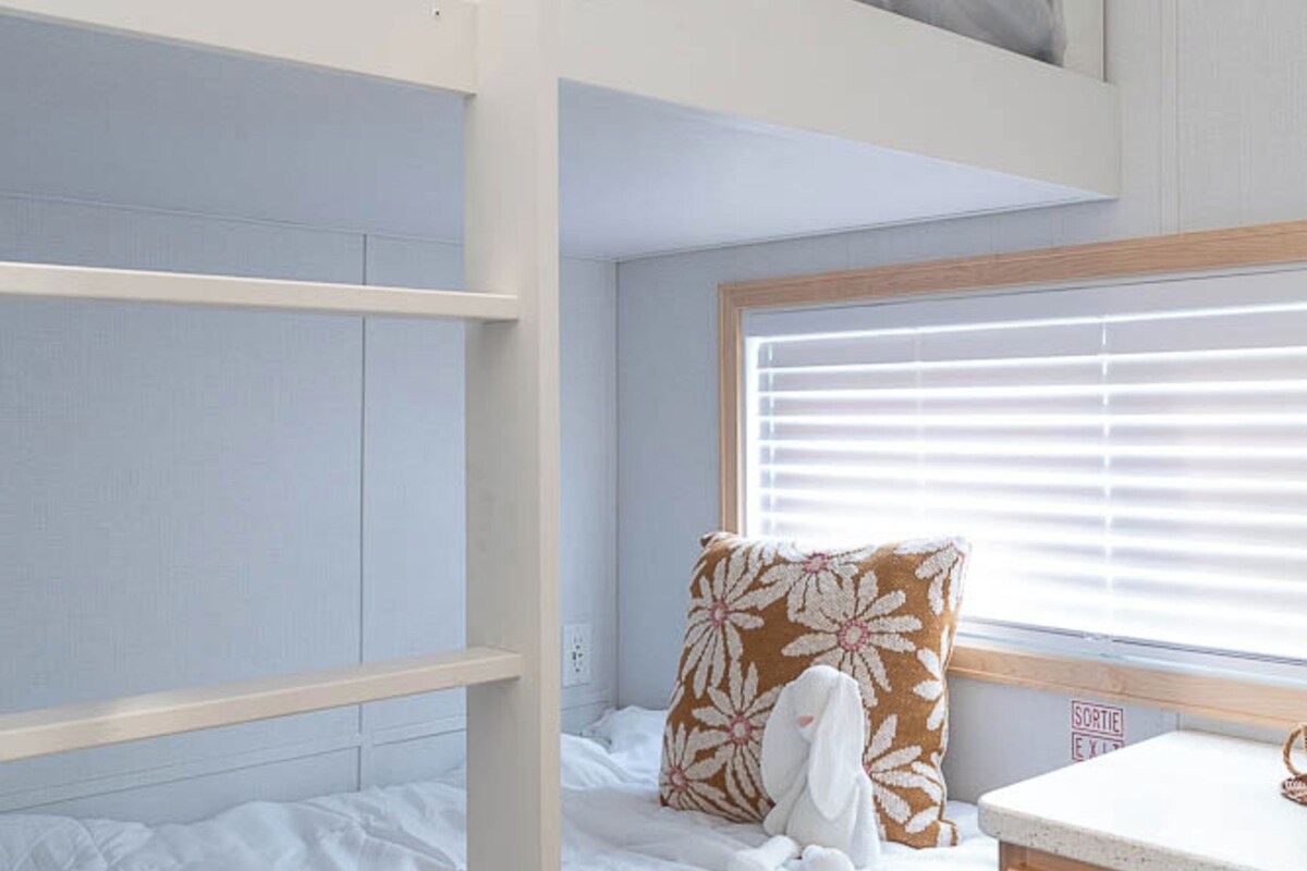 A bunk bed with a window, a bedside table, and a drawer unit.