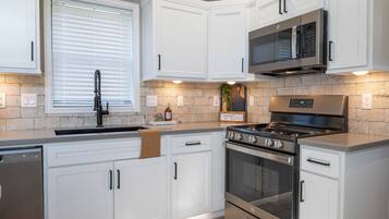 Una cocina moderna con muebles blancos, estufa de acero inoxidable y microondas.