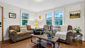 A living room with two leather sofas, a coffee table with books and a blue vase, and a view of greenery through the windows. - Creekside Cabin by Avantstay Creek Swims + Trout Fishing Firepit Deck Views Near Hunter Mtn (Jewett)