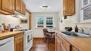A kitchen with wooden cabinets, a stove, a sink, and a window with a view of greenery. - Creekside Cabin by Avantstay Creek Swims + Trout Fishing Firepit Deck Views Near Hunter Mtn (Jewett)