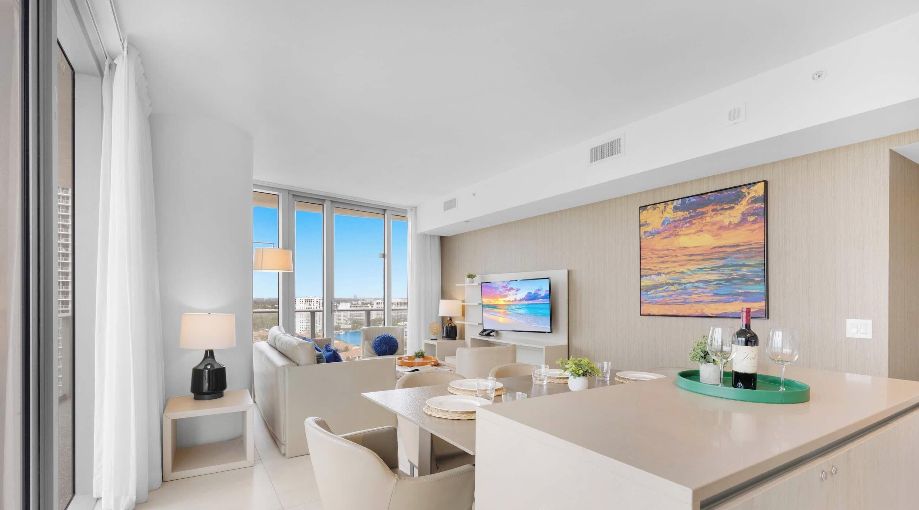 A modern hotel room with a large window, a flat-screen TV, a dining area, and a painting on the wall.