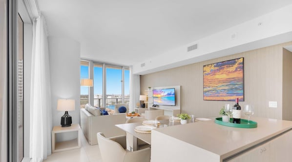 A modern hotel room with a large window, a flat-screen TV, a dining area, and a painting on the wall. - Oceanview Resort Stylish 2BR Balcony Bliss (Hollywood)