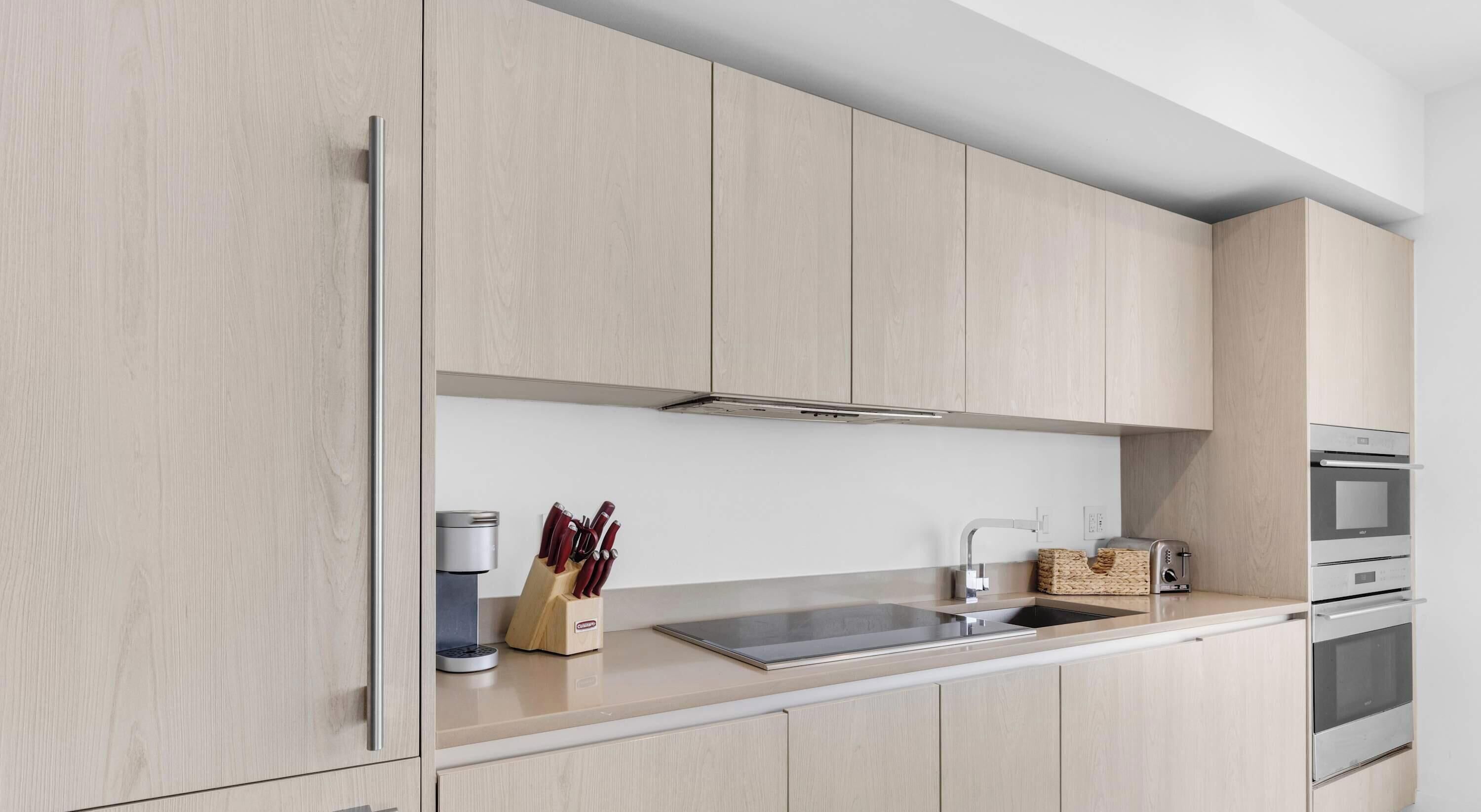 A modern kitchen with light wood cabinetry, a stainless steel sink, and a built-in oven.