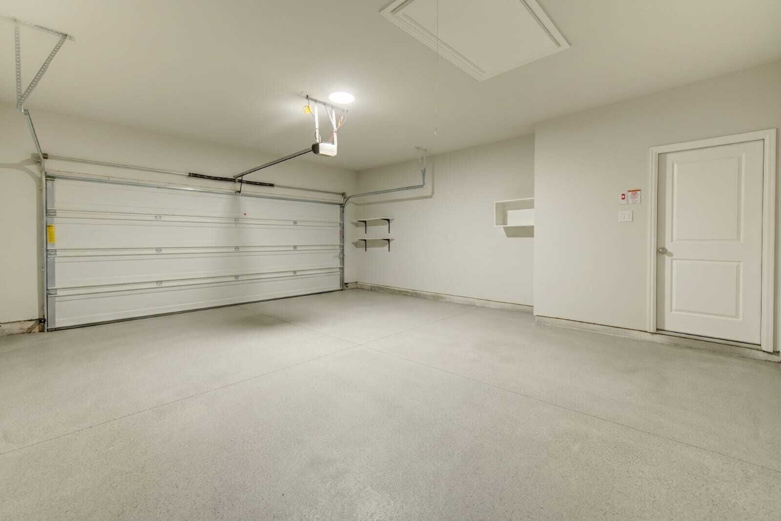 Eine saubere, leere Garage mit geschlossenem Garagentor, einer Deckenleuchte und einer weißen Tür rechts.