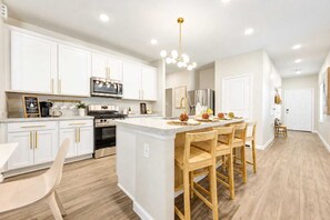 A modern kitchen with white cabinets, stainless steel appliances, and a central island with bar stools. - New! Modern FamGetaway near BigRivers, Sleeps 10 (Porter Heights)