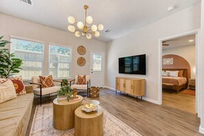 A modern living room with a sofa set, coffee tables, a TV, and a dining area. - New! Modern FamGetaway near BigRivers, Sleeps 10 (Porter Heights)