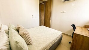 Ein Schlafzimmer mit einem Bett, Kissen, einem Holztisch und einer Tür.