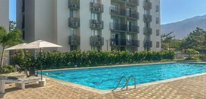 A swimming pool with a tiled deck, lounge chairs, and a view of a multi-story building with balconies. - Comfortable Apartment 2Bed/2Bath - Bello Horizonte - Santa Marta (Santa Marta)