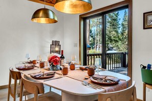 Comedor con una mesa grande dispuesta para cuatro personas, con sillas de madera y un florero central con flores.
