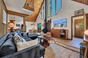 Ein geräumiges Wohnzimmer mit hoher Decke, Kamin, Essbereich und großem Fenster mit Blick ins Freie.