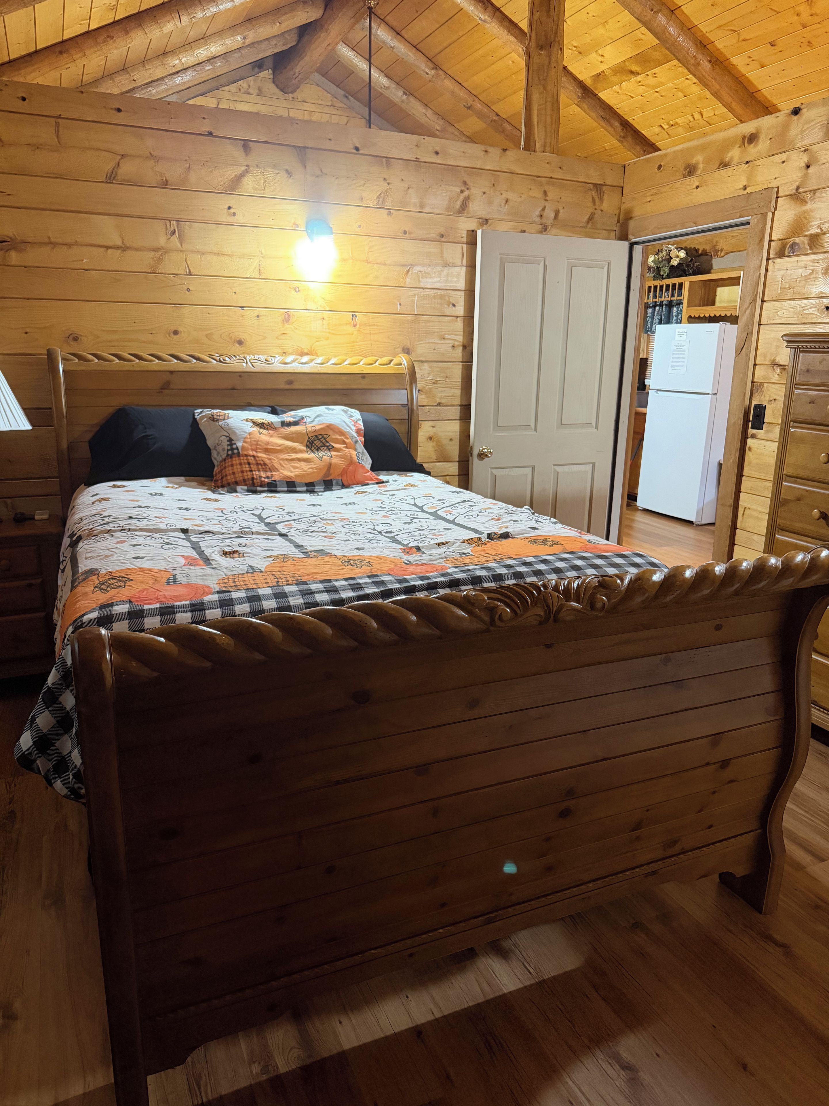 Une chambre à coucher dans une cabane en bois, comprenant un lit, une table de chevet, une commode et une porte donnant sur la cuisine.