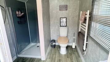 A compact bathroom with a shower, a toilet, and a window with blinds.