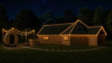 A wooden cabin with string lights, a barrel sauna, and a fire pit.