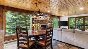 Een houten interieur met een stenen open haard, een eettafel met stoelen en een bank.