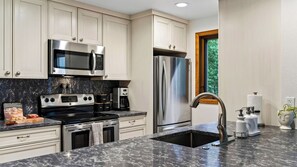 A modern kitchen with stainless steel appliances, a marble countertop, and a view of the outdoors through a window. - Falls & Firs by Avantstay Mtn Views + Balcony Trailheads + Ski Bus (Vail)