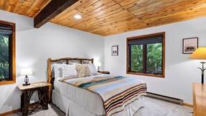 A bedroom with a wooden ceiling, a bed with a striped blanket, two bedside lamps, and a window with a view of trees. - Falls & Firs by Avantstay Mtn Views + Balcony Trailheads + Ski Bus (Vail)