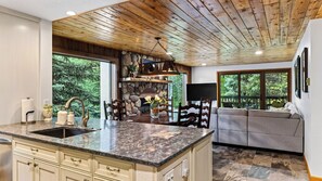 A modern kitchen with a granite countertop, wooden ceiling, and a stone fireplace. - Falls & Firs by Avantstay Mtn Views + Balcony Trailheads + Ski Bus (Vail)