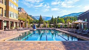 A swimming pool with lounge chairs and umbrellas, surrounded by buildings and mountains.