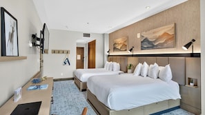 A hotel room with two beds, a desk, a chair, a TV, and artwork on the walls.
