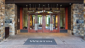 A hotel entrance with double doors, a stone facade, and a welcome mat with the hotel's name.