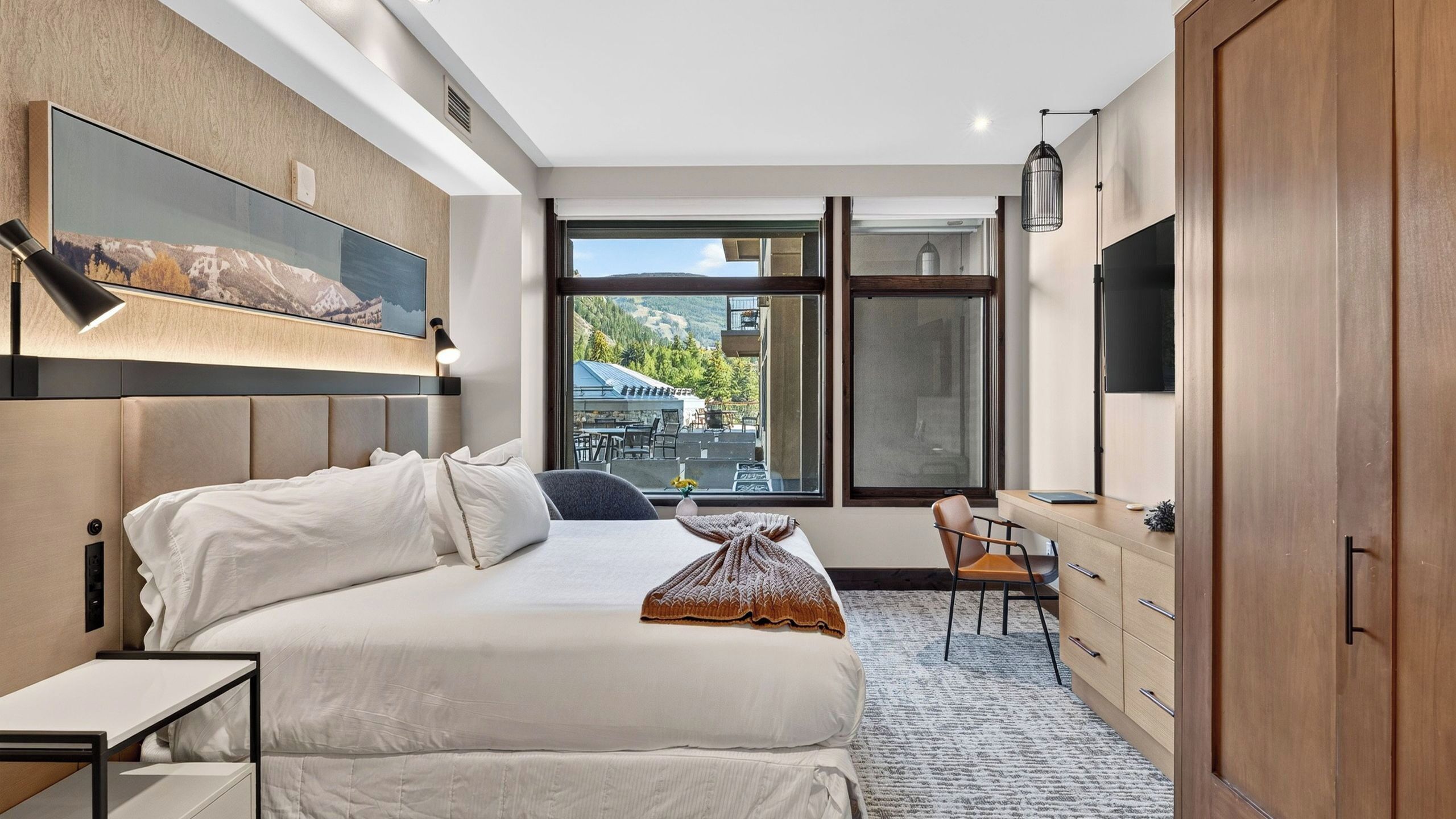 Habitación de hotel moderna con una cama grande, un escritorio y vistas al exterior.