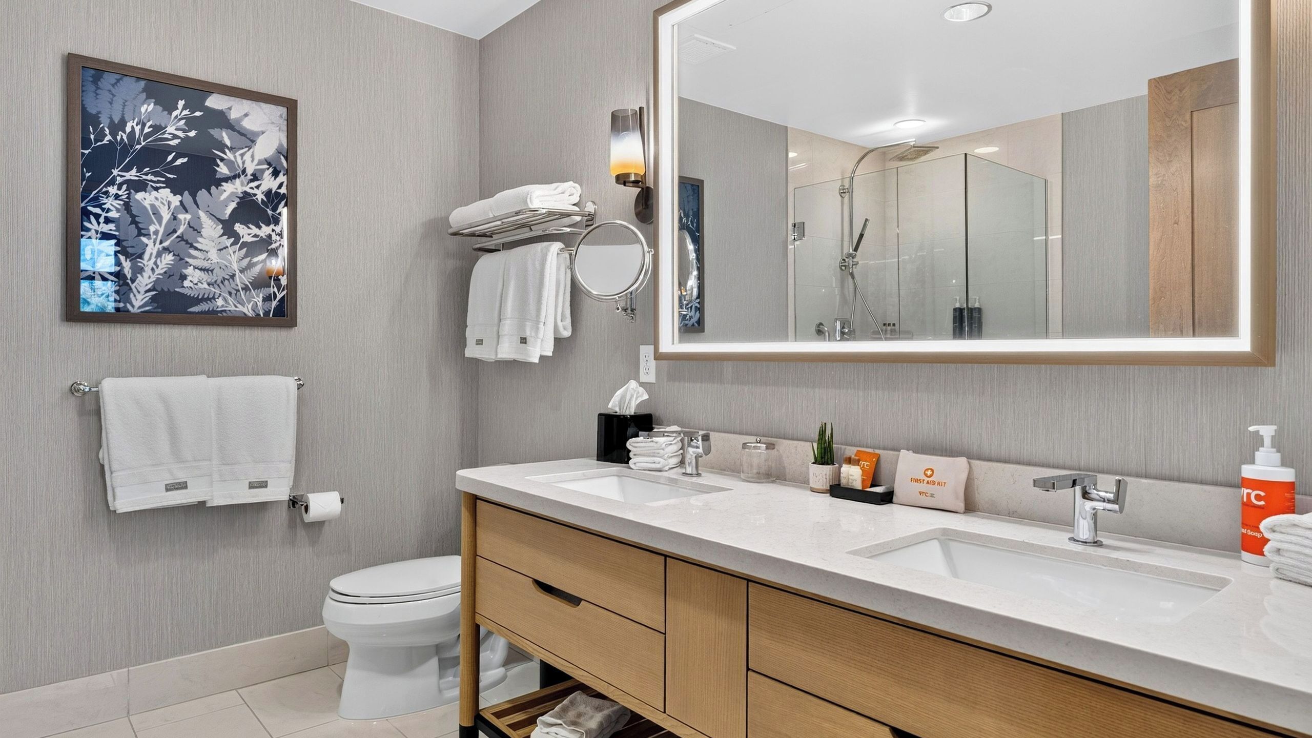 Une salle de bain moderne avec un grand miroir, deux lavabos, des toilettes et un porte-serviettes.