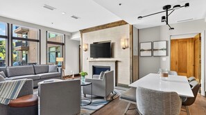 Ein modernes Wohnzimmer mit Kamin, einem flachbildfernseher darüber und einem Essbereich mit Tisch und Stühlen.
