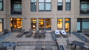 Ein Terrassenbereich im Freien mit Sitzgelegenheiten, einem Esstisch und Blick ins Gebäudeinnere durch die Fenster.