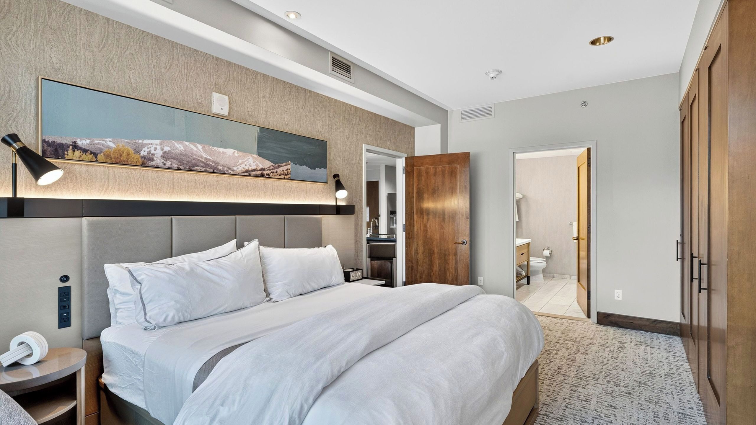 A modern hotel room with a large bed, a mounted TV, and a walk-in closet.