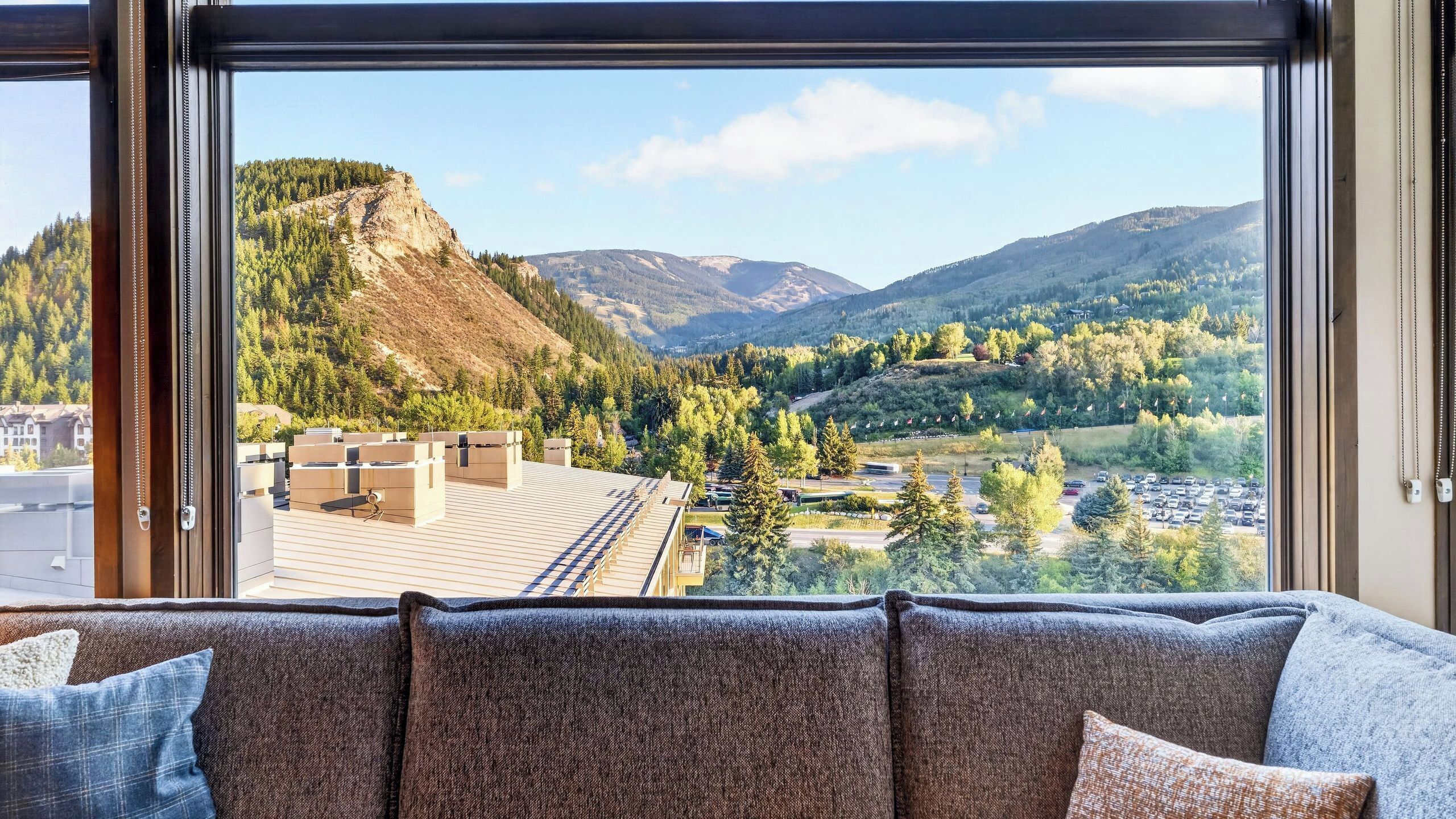 A room with a large window offering a view of a mountainous landscape, a sofa with multiple cushions, and a door with a chain.