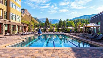 A swimming pool with lounge chairs and umbrellas, surrounded by buildings and mountains.