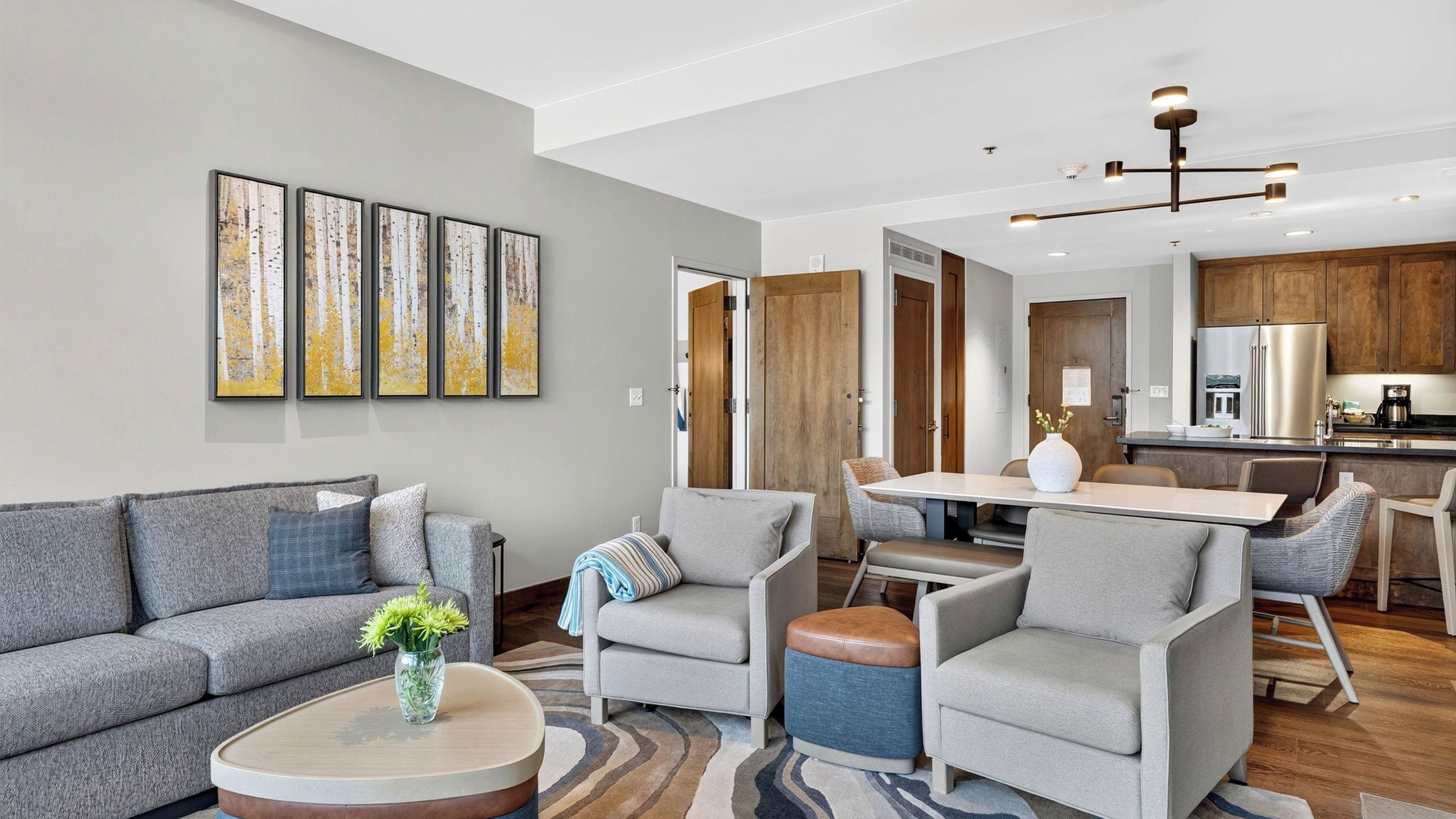 A modern living room with a sofa, armchairs, a coffee table, and a dining area with a table and chairs.