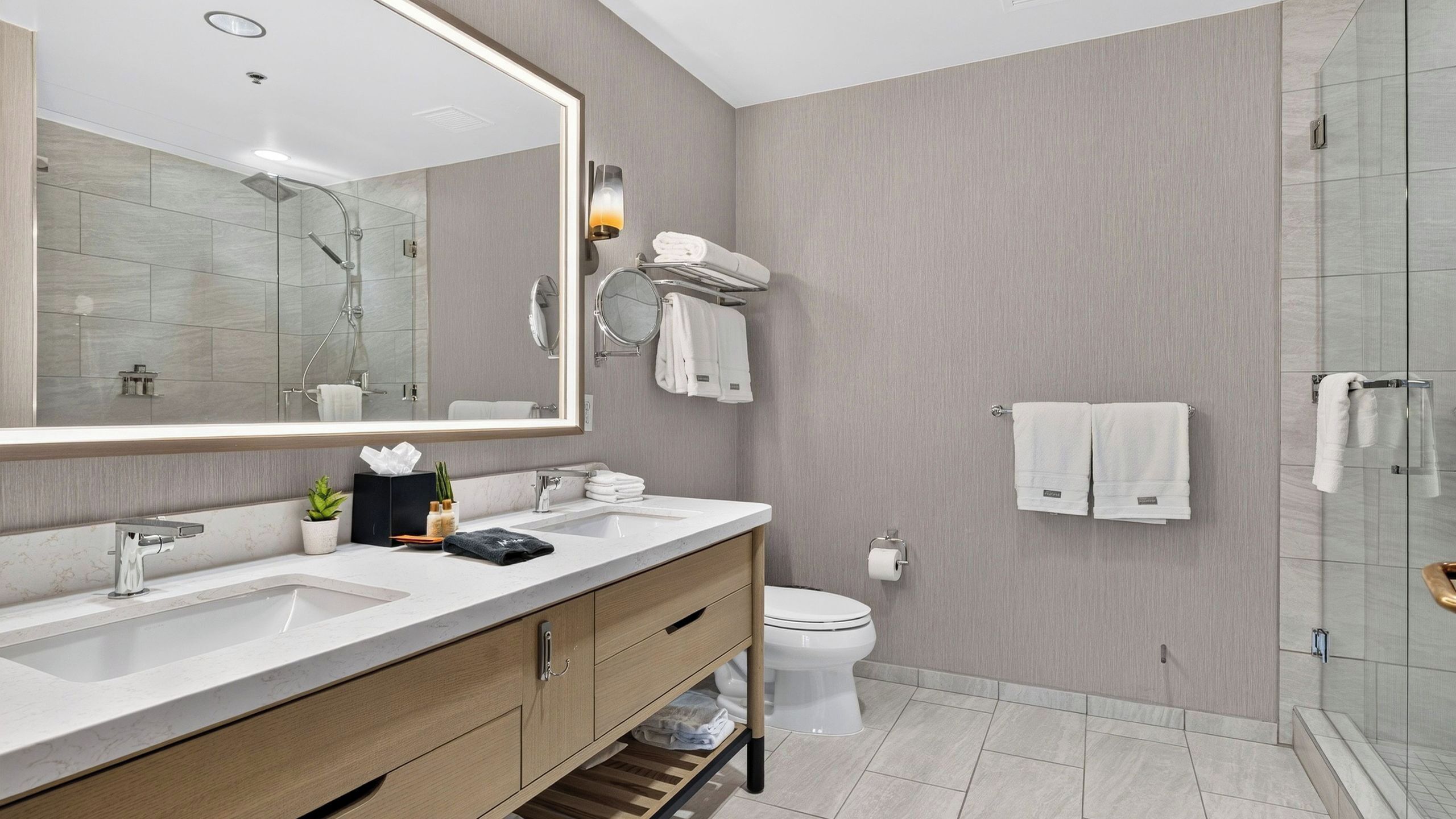 Een moderne badkamer met een wastafelmeubel met dubbele wastafel, een toilet, een douchecabine van glas en een grote spiegel.