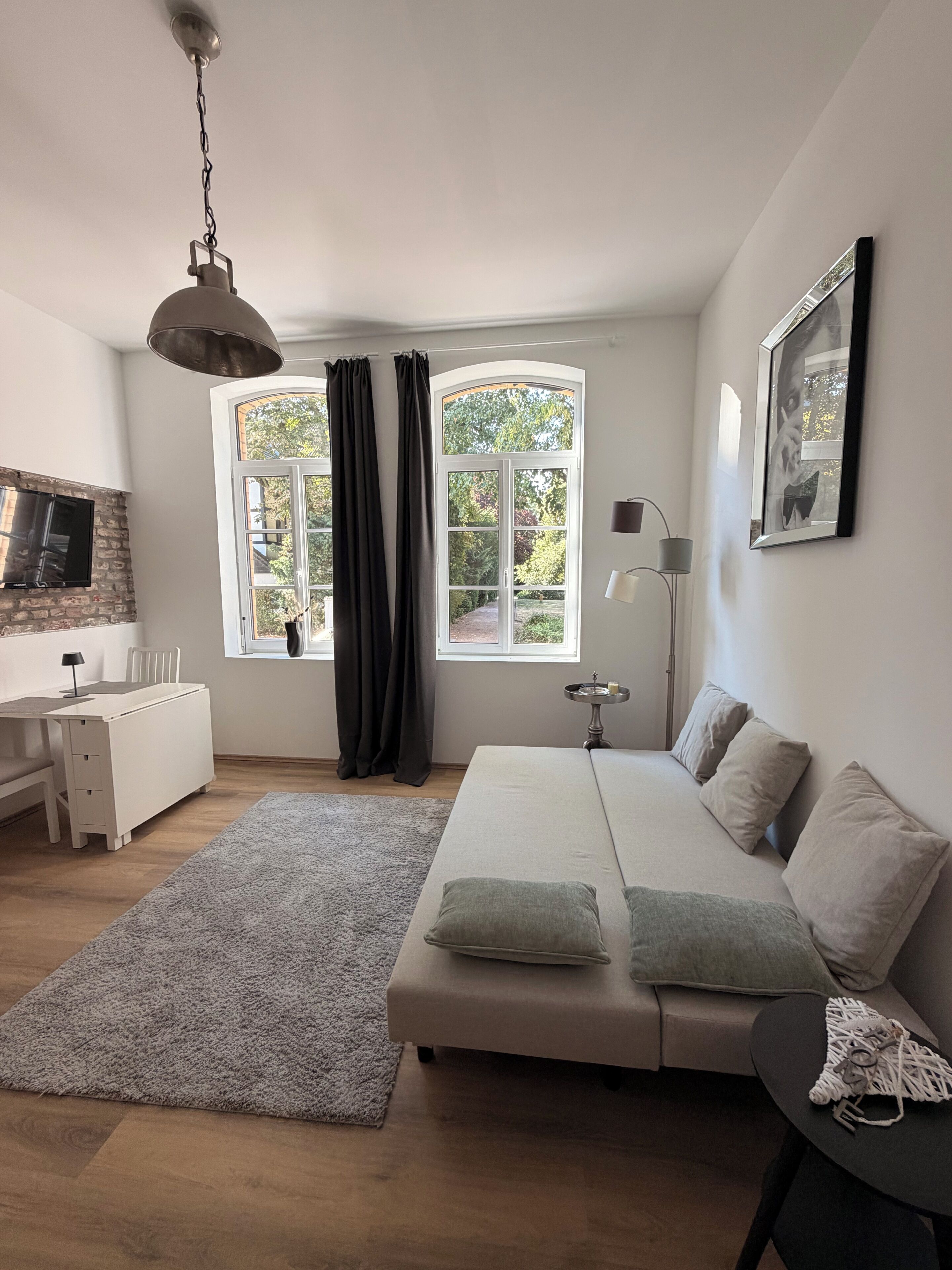 Une chambre moderne avec un lit, une table de chevet, une lampe et une vue sur la verdure à l’extérieur.