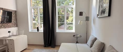 Une chambre moderne avec un lit, une table de chevet, une lampe et une vue sur la verdure à l’extérieur.