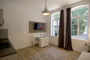 A room with a white desk, a chair, a television mounted on a brick wall, a window with curtains, and a hanging light fixture. - Completely renovated apartment in an older building in the heart of Ratingen with excellent transportation access (Ratingen)