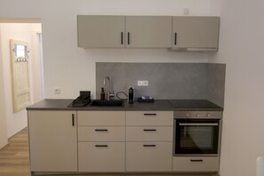 Eine kleine Küche mit Einbauofen, Spüle und einer Arbeitsplatte mit Kaffeemaschine und Flasche.