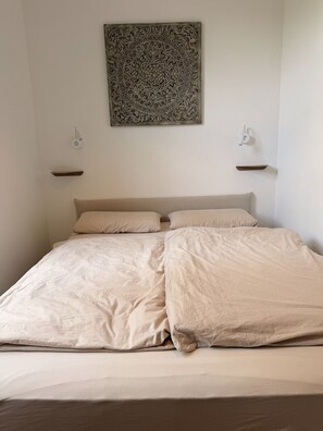 A bedroom with a bed, two bedside tables, and a decorative wall piece. - Completely renovated apartment in an older building in the heart of Ratingen with excellent transportation access (Ratingen)