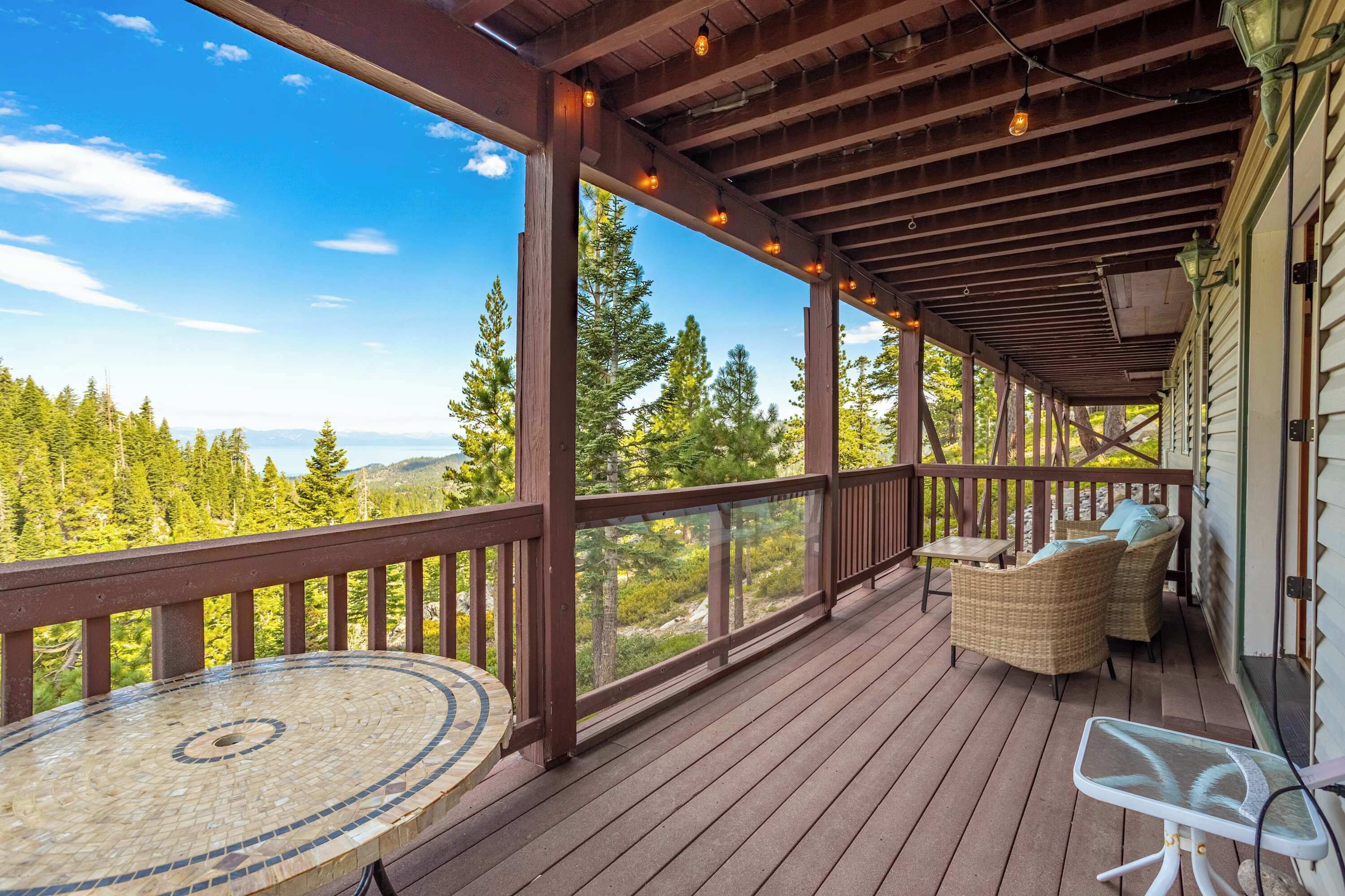 Une terrasse en bois avec une table et des chaises en verre, donnant sur un paysage boisé.