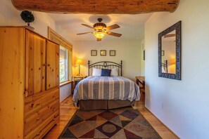 Une chambre à coucher avec un lit, une armoire en bois, un ventilateur de plafond et un tapis à motifs.