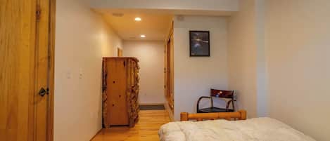 Un dormitorio con un armario de madera, una cama con una colcha estampada, una silla y un cuadro en la pared.