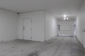 Un pasillo limpio y vacío con paredes blancas y suelo de hormigón, que conduce a una puerta cerrada al final.