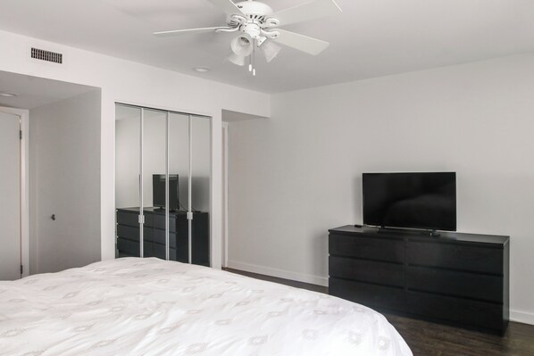 Un dormitorio con cama, cómoda, televisor y ventilador de techo.