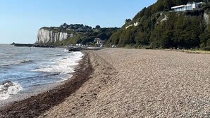A pebble beach with a cliff and houses in the background. - The Hollies (Walmer)