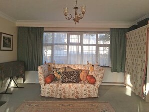 Un salon avec un canapé à motifs floraux, un lustre et une grande fenêtre avec des rideaux.