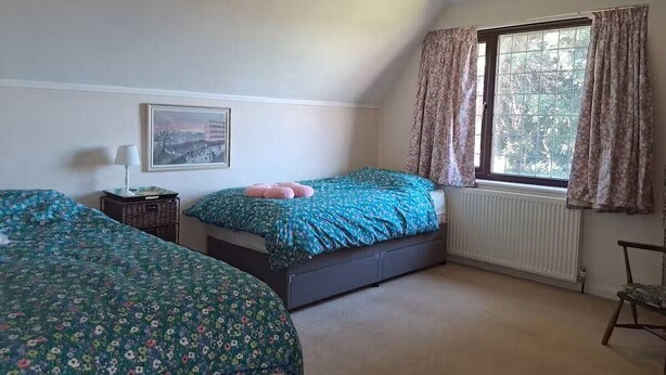 A bedroom with two beds, a window with curtains, a radiator, and a hanging light fixture. - The Hollies (Walmer)