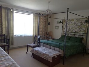 Une chambre à coucher avec un lit à baldaquin, une chaise, une petite table et une fenêtre avec des rideaux.