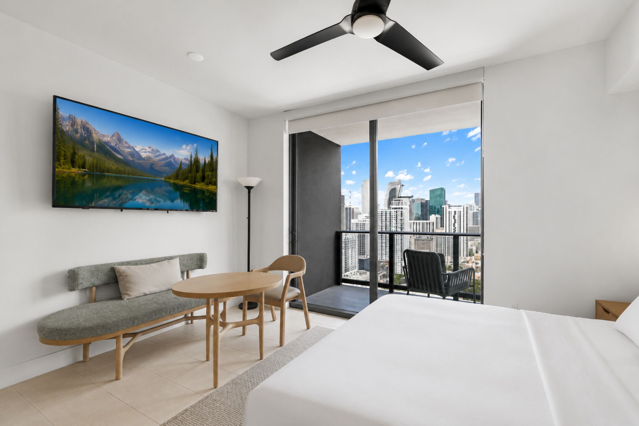 Une chambre moderne avec vue sur la ville, comprenant un grand lit, un canapé, une table à manger et un ventilateur de plafond.
