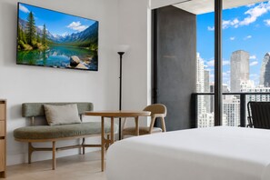 Ein modernes Hotelzimmer mit einem großen Bett, einer Couch, einem kleinen Tisch und einem Sessel. An der Wand hängt ein Gemälde einer Berglandschaft.